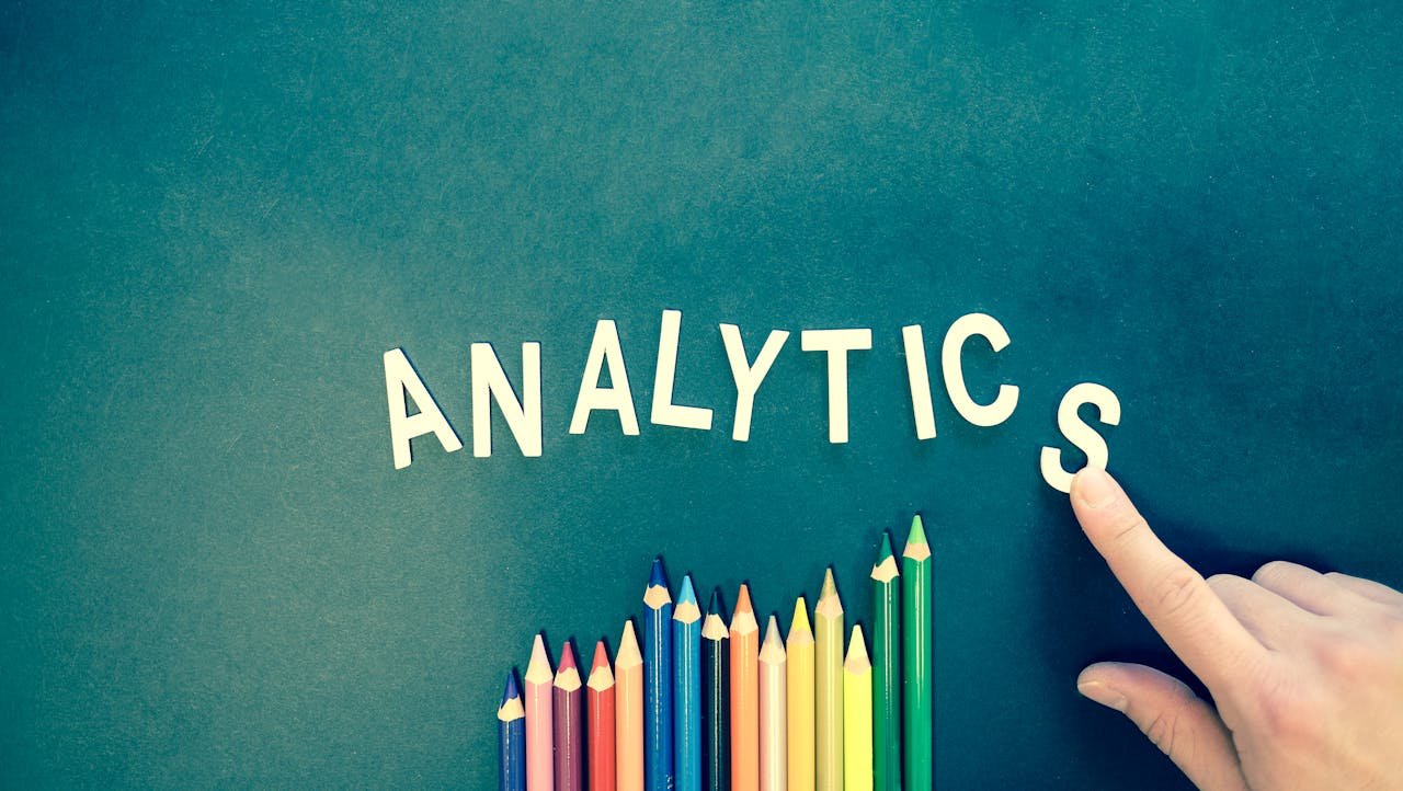 who-we-are Colored pencils and letters spelling 'ANALYTICS' on a textured background with a hand.